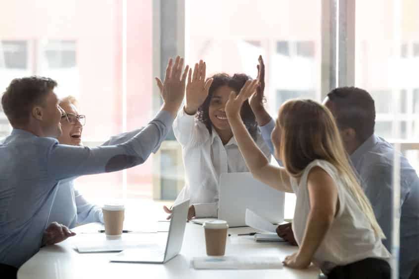 un groupe de personnes assises autour d'une table, les mains en l'air